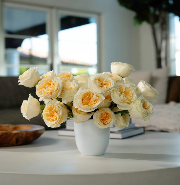 Bouquet of white and yellow roses in a white vase on a table.