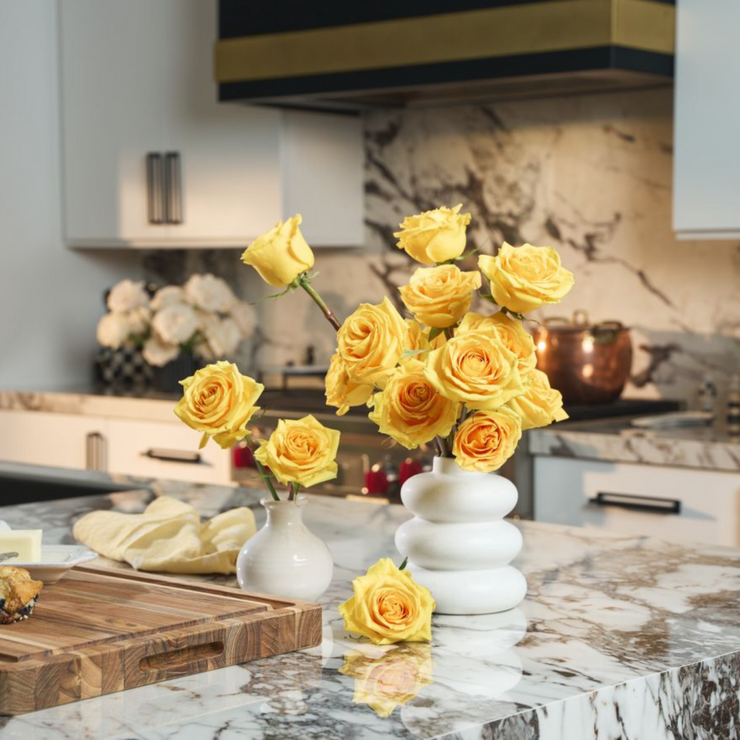 Yellow roses in a white vase on a kitchen counter with a marble backsplash.