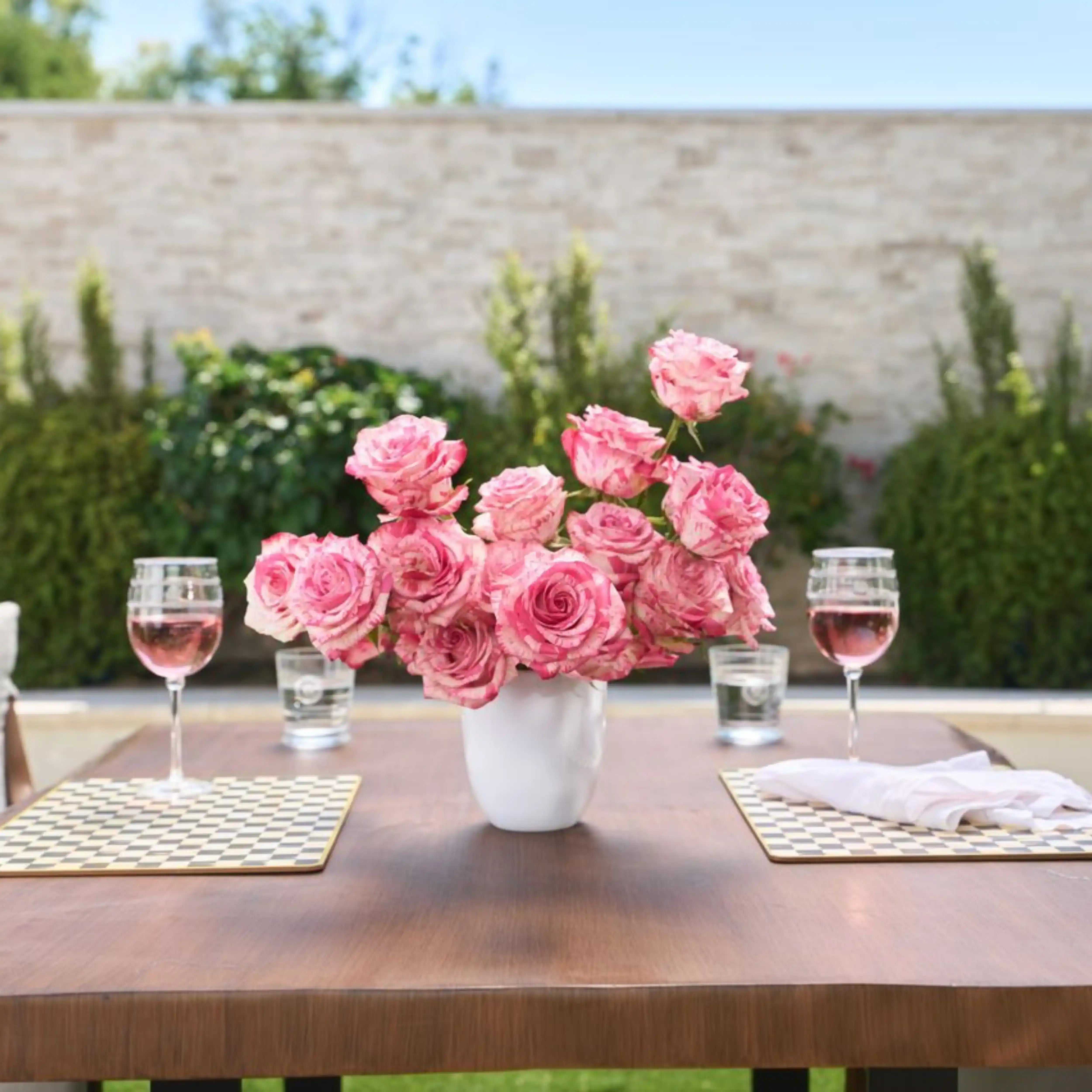 Pink roses in a vase on a wooden table with wine glasses and water glasses outdoors.