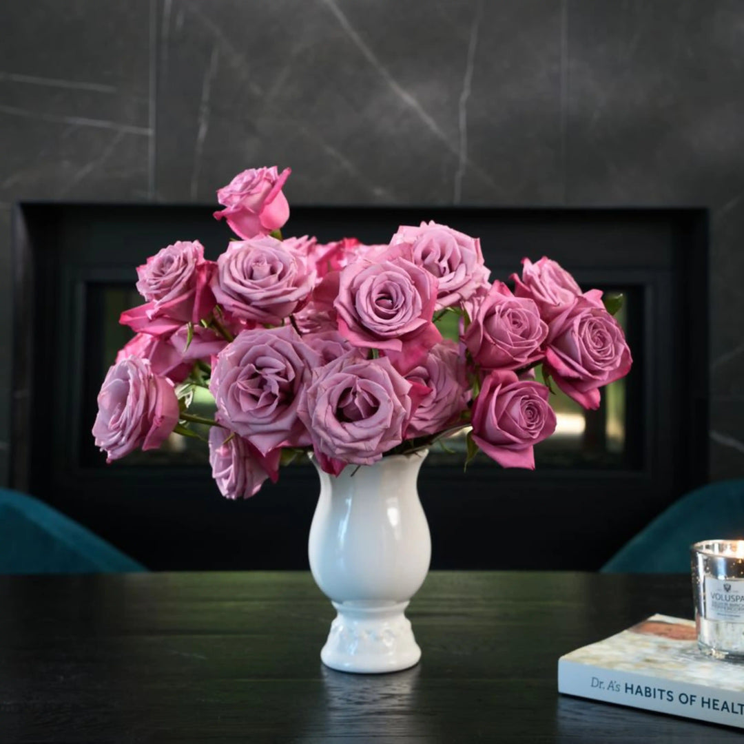 Bouquet of pink roses in a white vase on a dark surface with a blurred background