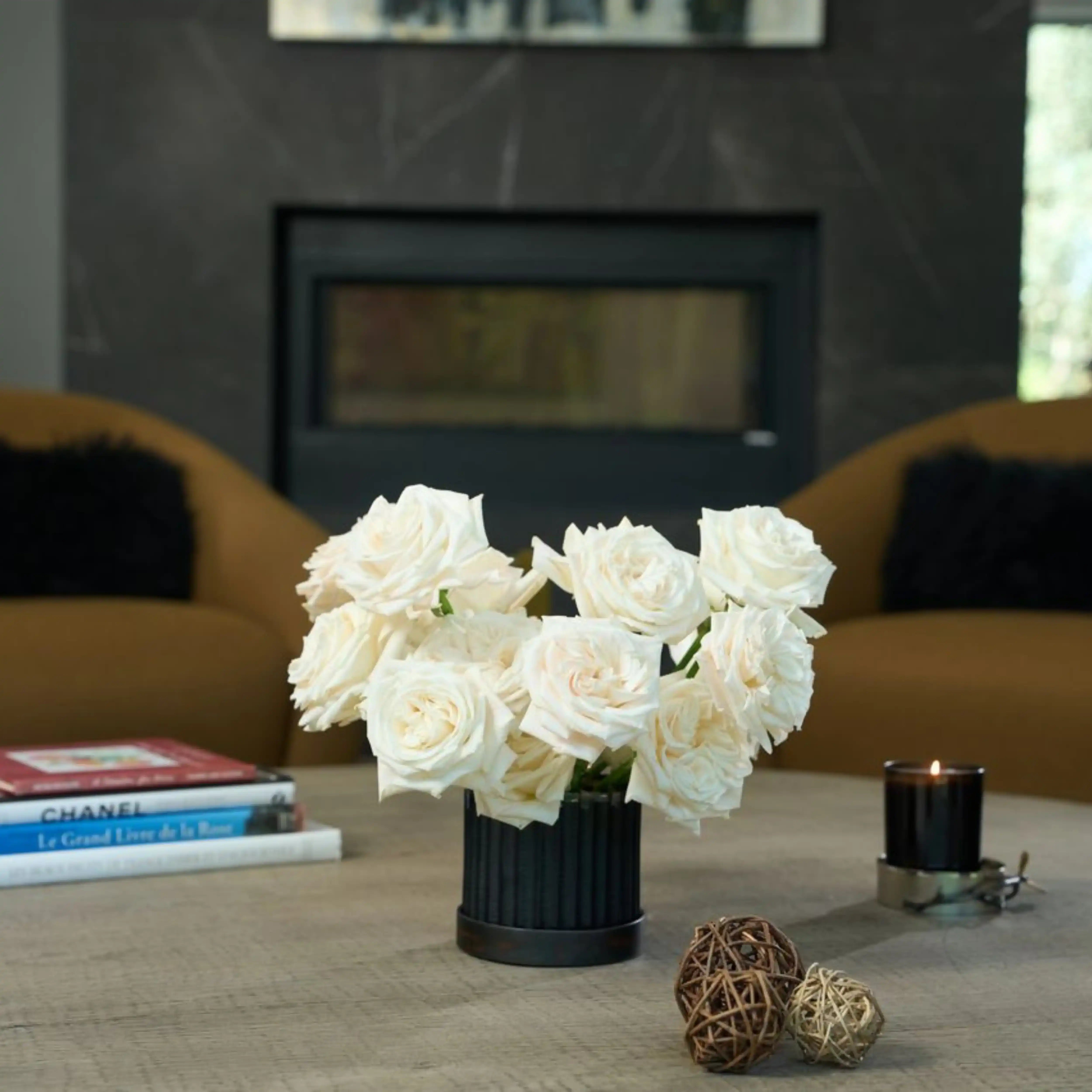 White roses in a vase on a coffee table with books and a candle in the background.