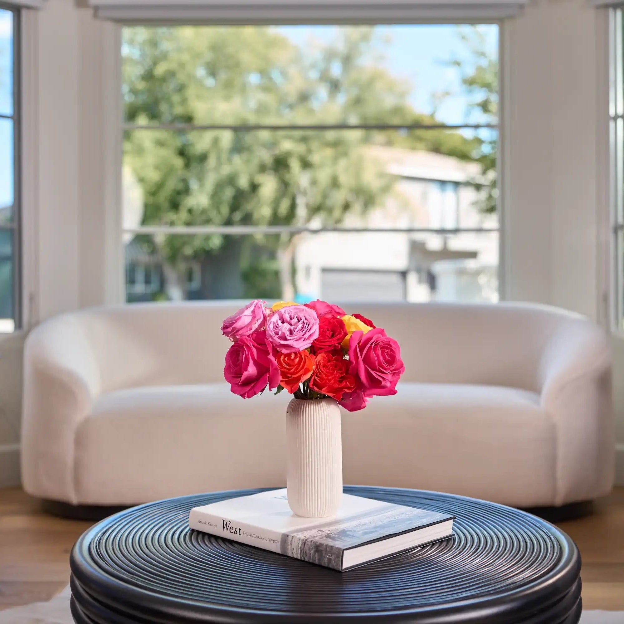 Modern living room with a white sofa, gray chairs, and a round black coffee table with a floral arrangement.