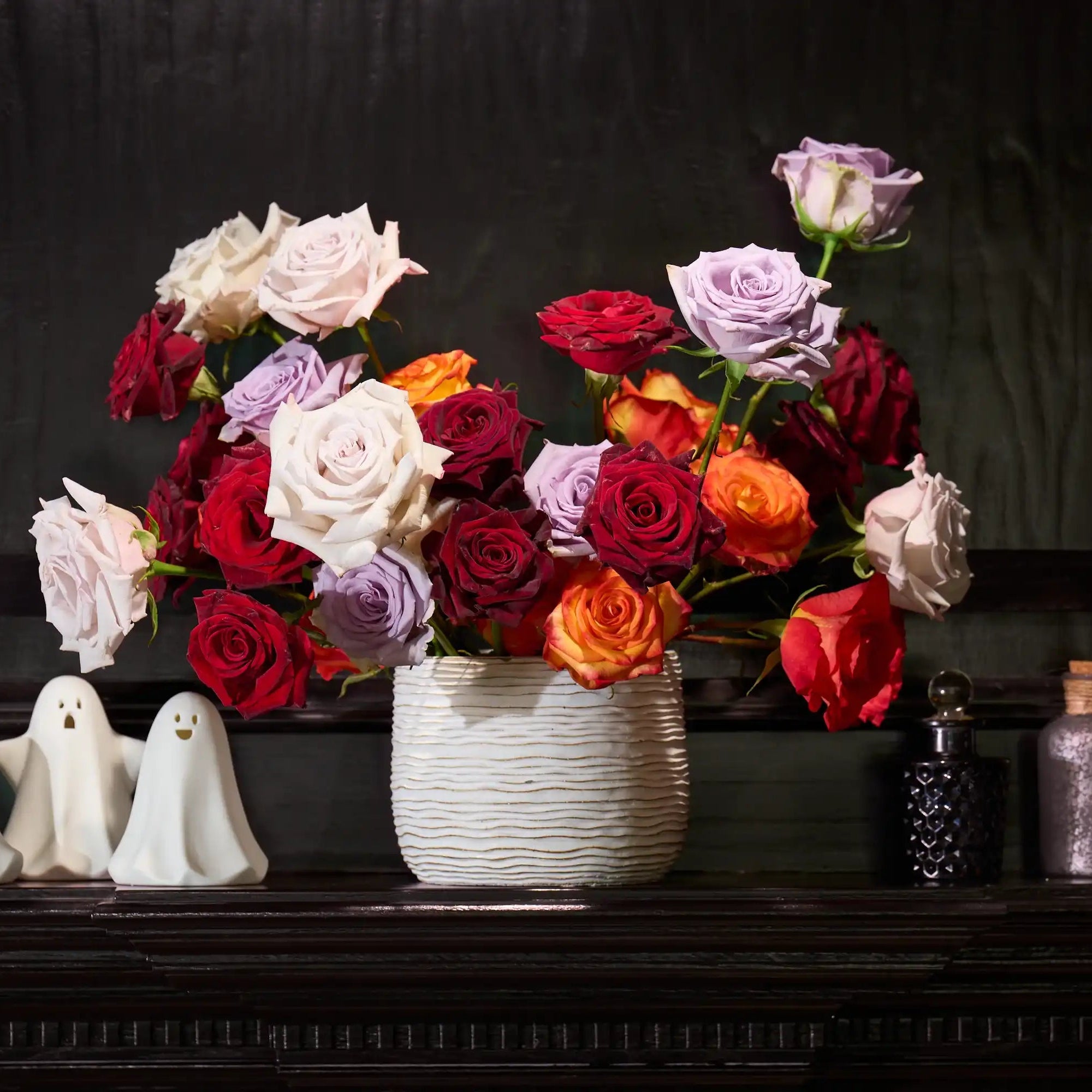 Colorful bouquet of flowers in a vase on a dark surface with Halloween-themed decorations.