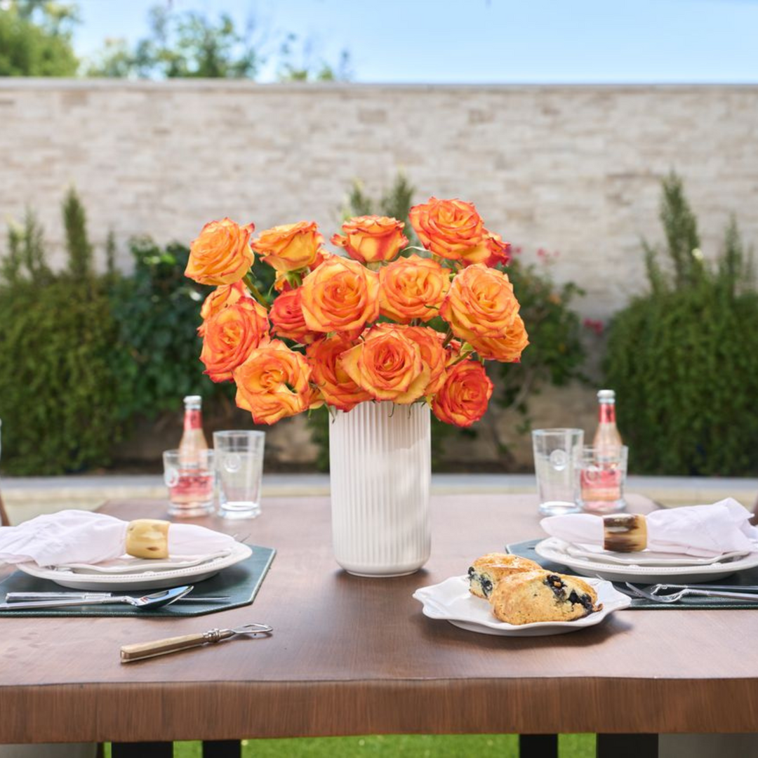 Outdoor table setting with orange roses in a vase, glasses, and pastries.
