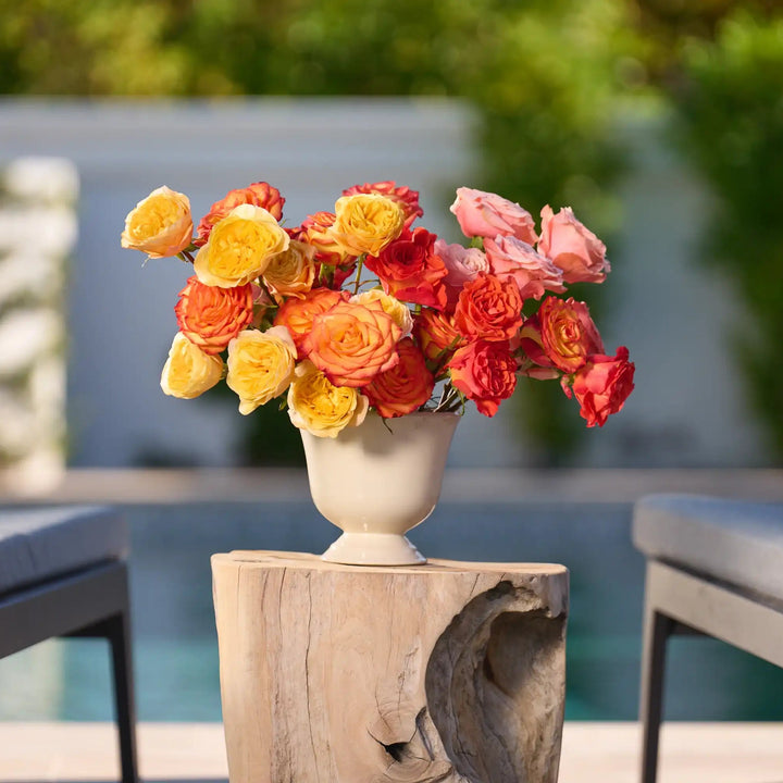 Bouquet of colorful flowers in a vase on a wooden stand with chairs and a blurred background