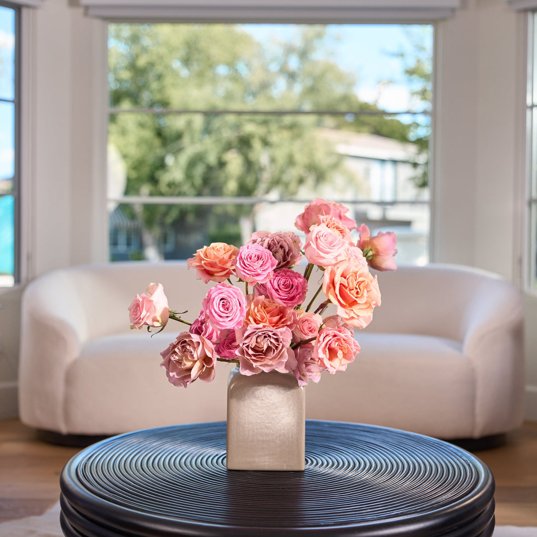 Floral arrangement on a table in a modern living room with large windows.