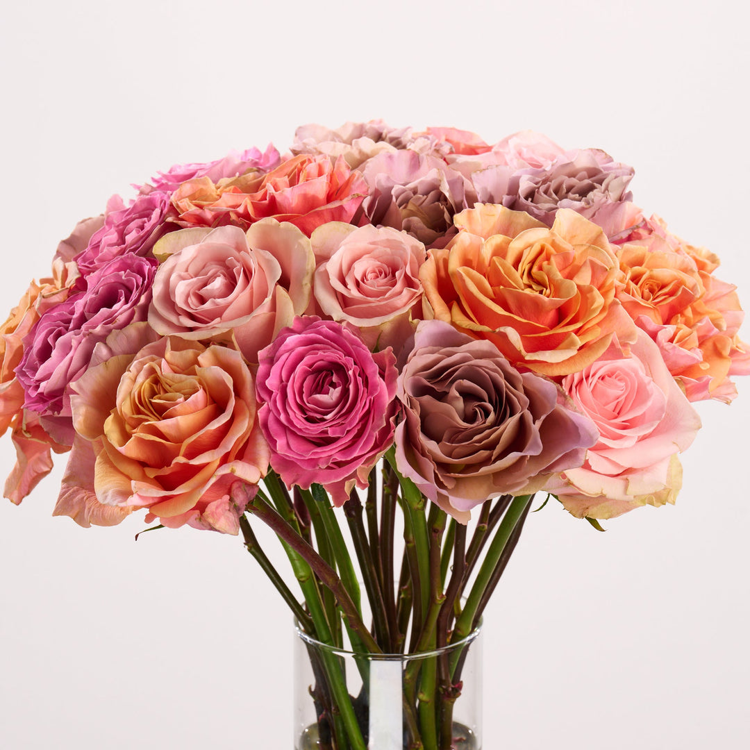 Bouquet of pink and orange roses in a clear vase on a light background