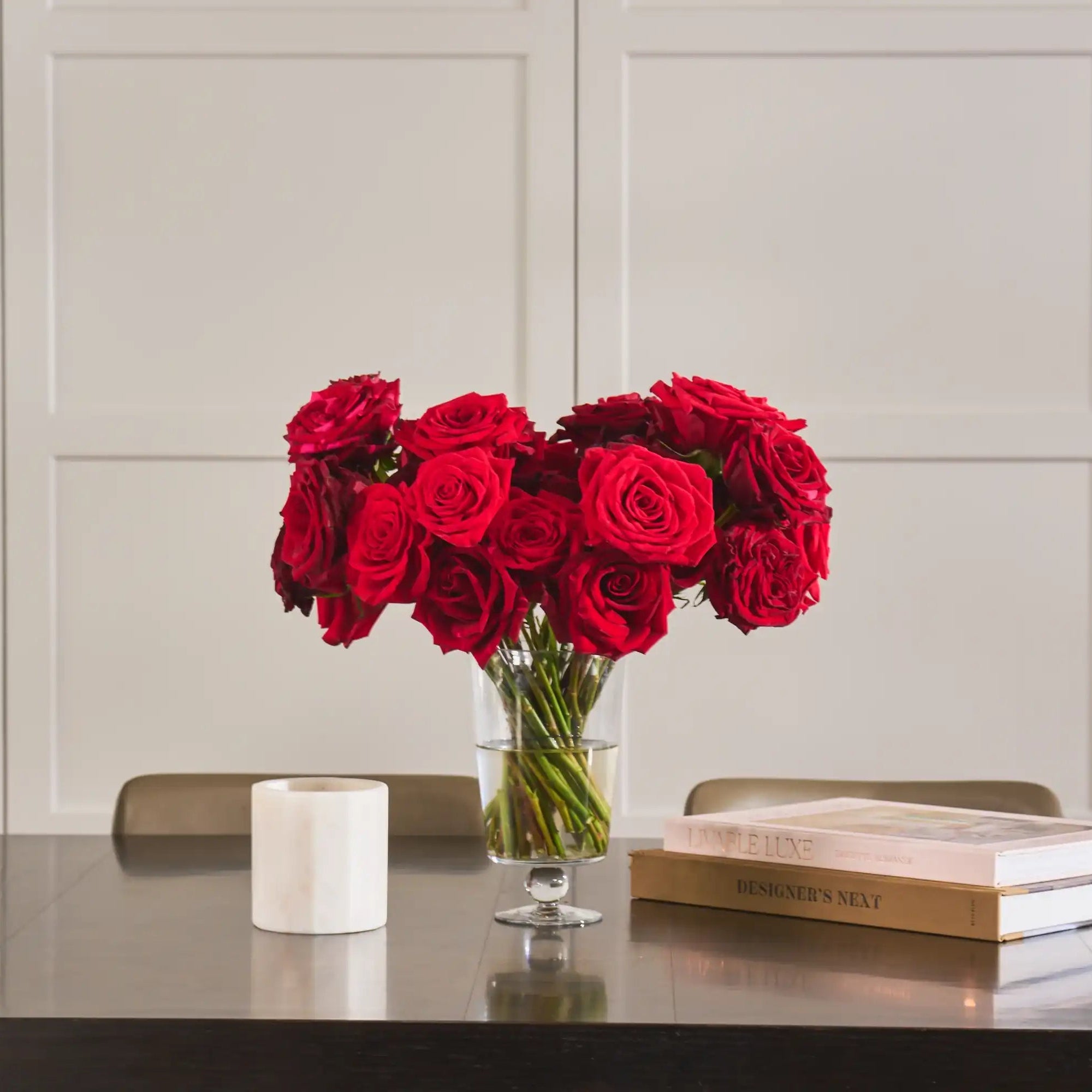 Bouquet of red roses in a glass vase on a table with books and a candle.