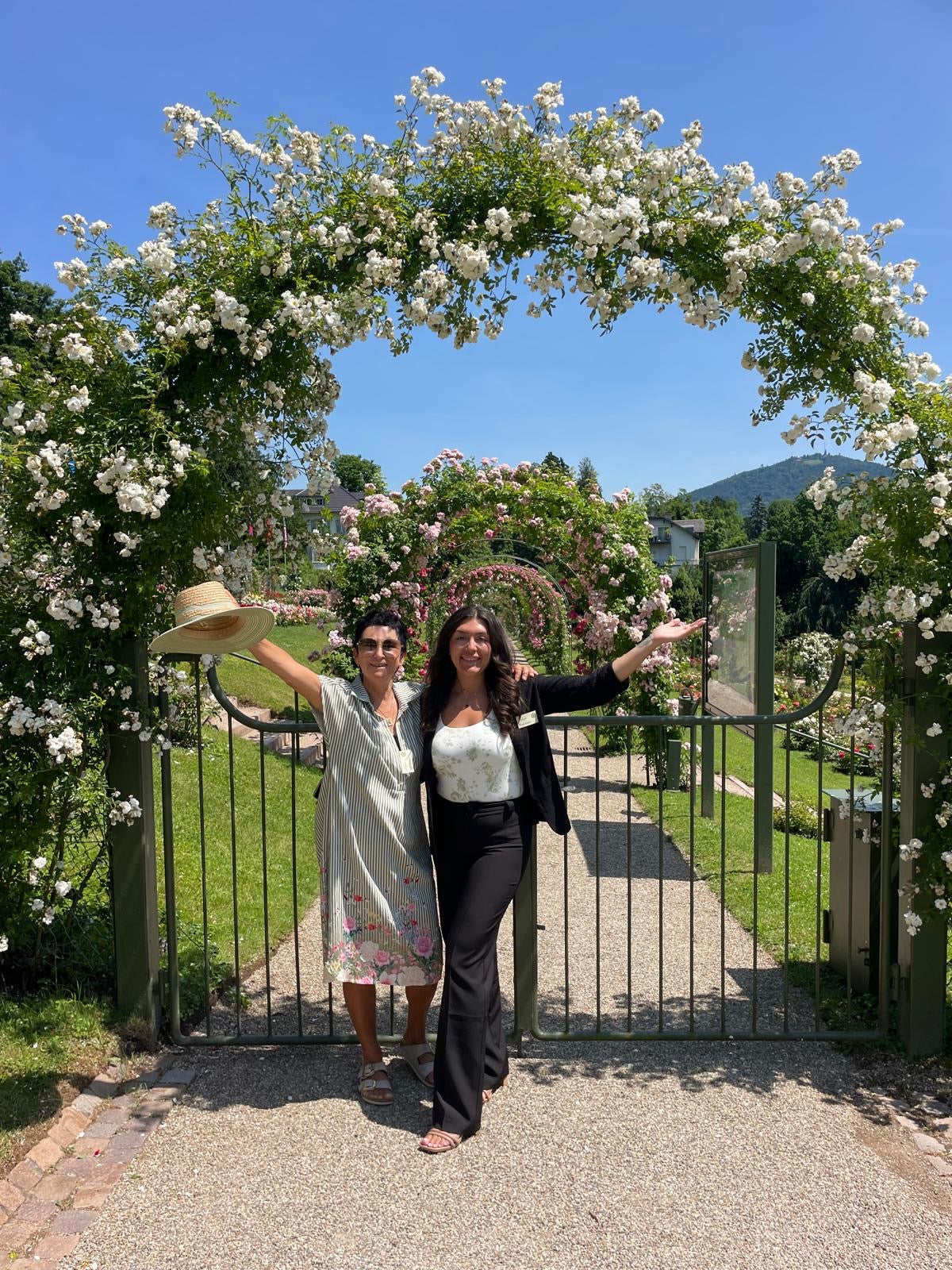 Two women standing under a floral archway in a garden.