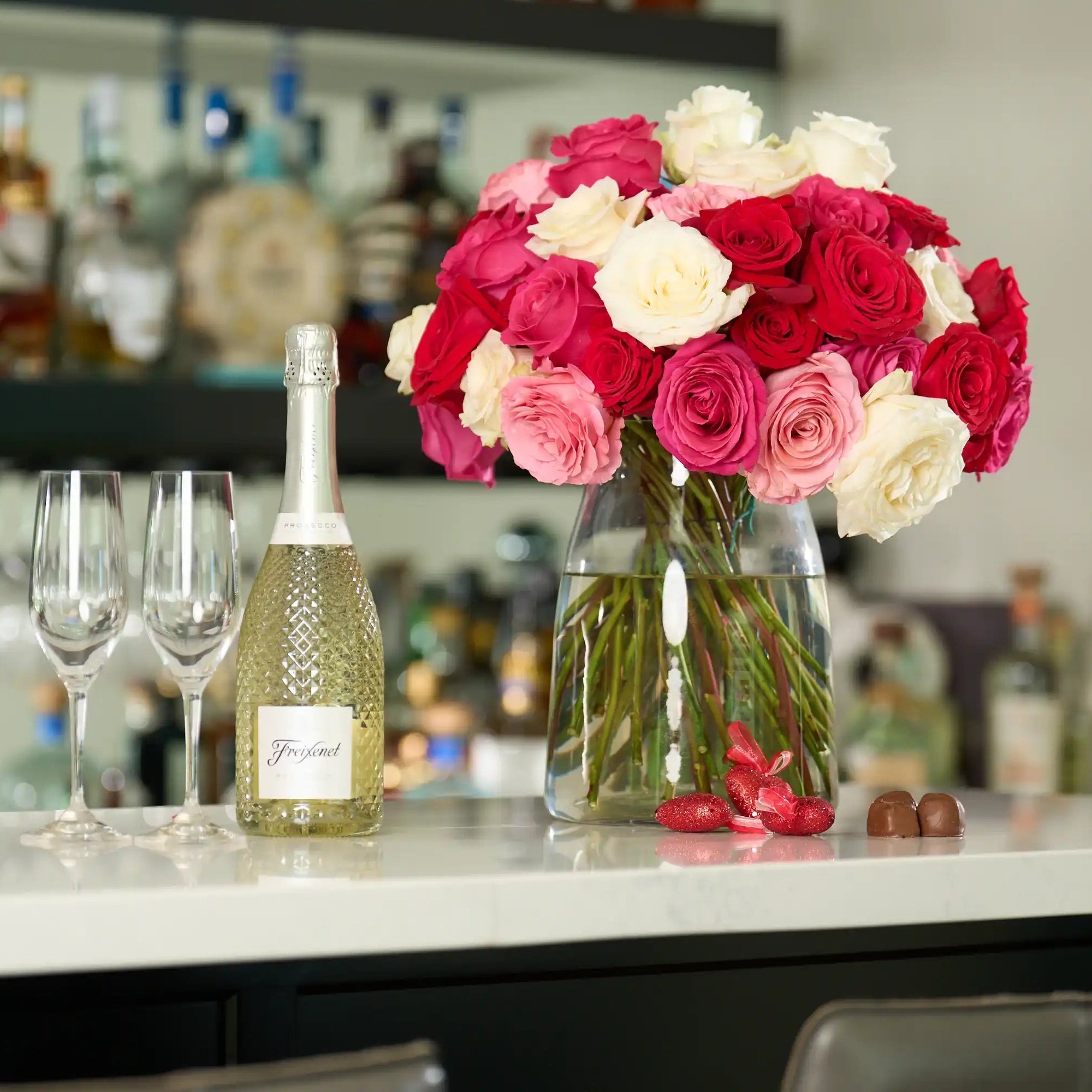 Bouquet of red and white roses in a vase on a bar counter with champagne bottle and glasses.
