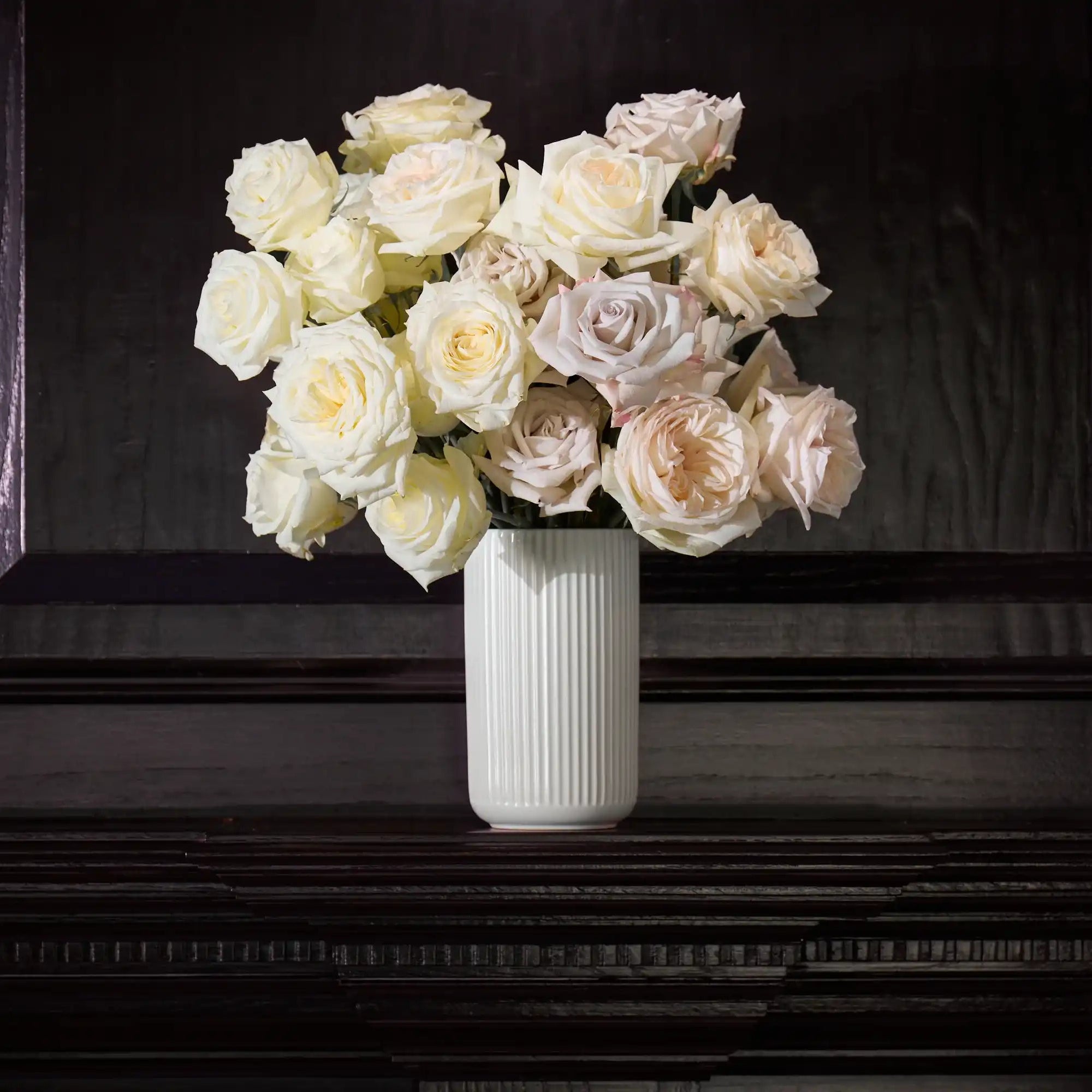 White roses in a vase on a dark surface with a black frame.