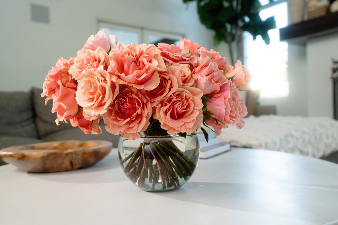 Bouquet of pink flowers in a clear vase on a table with a blurred indoor background